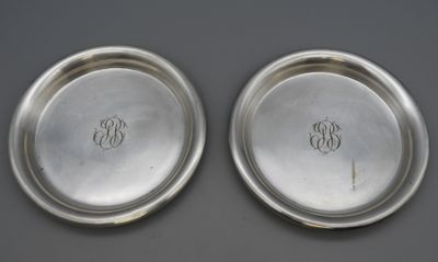 two silver plates with initials on them sitting on a table