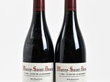 two bottles of red wine sitting next to each other on a white surface