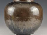 un vase brun et noir posé sur une surface blanche