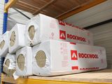 Plusieurs rouleaux de laine de roche sont empilés sur une étagère dans un local de stockage
