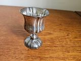 a silver cup on a wooden table with a white wall in the background