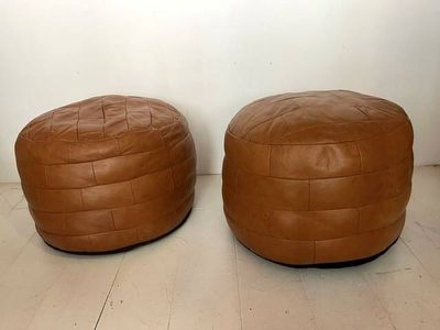 two brown leather ottomans sitting on top of a wooden floor