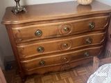 a dresser with a lamp on top of it next to a bed