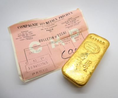 un vieux lingot d'or posé à côté d'un bout de papier sur une surface blanche
