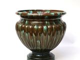 a brown and green vase sitting on a white surface