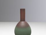 a green and brown vase sitting on a white surface