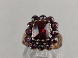 a close up of a ring with a red stone surrounded by garnets