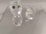 figurines en cristal représentant un chat et un hibou posés sur une table en verre