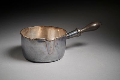 une casserole en argent avec un manche en bois posée sur une table
