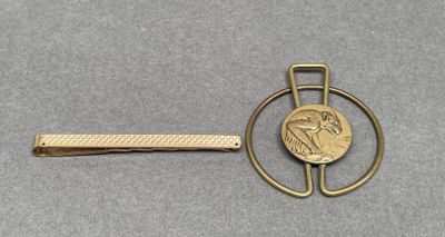 a gold tie bar with a coin on it