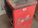 une glacière rouge posée dans un garage, avec des outils dessus
