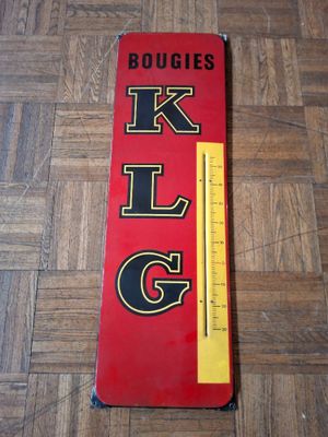 une pancarte rouge et noire portant l'inscription « klg », posée sur un plancher en bois