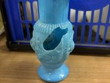 a blue vase sitting on a table with a basket in the background