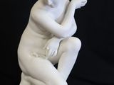 white marble statue of a woman sitting on a pedestal with her hands on her knees