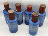 six bottles of blue paint with brown caps on a white surface