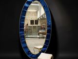 an oval mirror with a blue frame and a stool in front of it