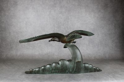 sculpture en bronze représentant un oiseau sur une vague, sur fond gris