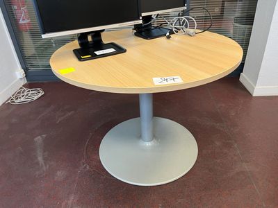 Table circulaire monopode, dessus en mélaminé clair.