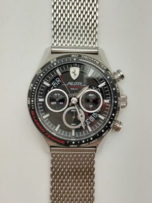 montre argentée avec cadran noir et bracelet en mailles argentées sur fond blanc