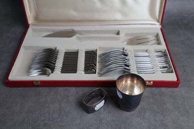 des couverts dans un coffret rouge posé sur une surface grise, comprenant une cuillère en argent et une tasse en argent