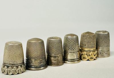 six antique thimbles lined up in a row on a white surface