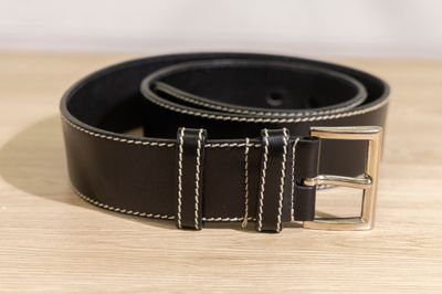 black leather belt with silver buckle on a wooden surface