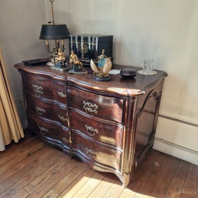 une commode placée dans un coin de la pièce, sur laquelle est posée une lampe