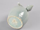 a green vase with a bird on it on a gray surface