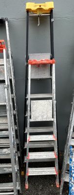 several ladders are lined up against a gray wall in front of a building