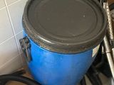 a blue barrel with a black lid sitting next to a black hose