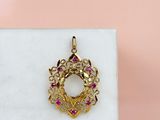 a close up of a gold pendant with pink stones on a marble surface