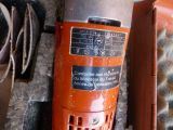 an orange electric drill on the ground next to a piece of wood