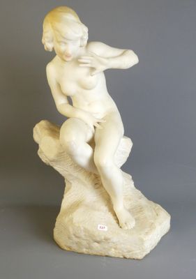 une statue en marbre blanc représentant un garçon assis sur un rocher