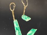 trois boucles d'oreilles en jade vert et or sur un fond noir