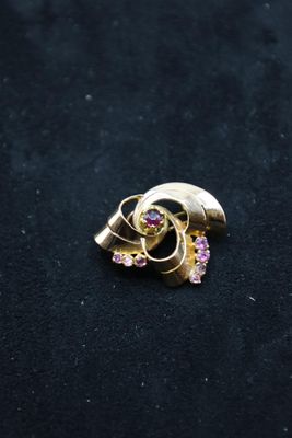 a close up of a gold brooch with pink stones on a black surface