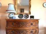 une commode surmontée d'un miroir, dans une pièce où des assiettes sont accrochées au mur
