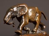 bronze statue of an elephant walking on a rock with its trunk in the air