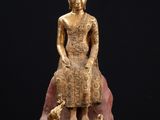 une statue en or représentant une personne assise sur un rocher avec un chien