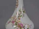 a white vase with a gold base and a pink flower on it