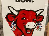 affiche représentant une vache rouge au visage souriant devant un mur de briques