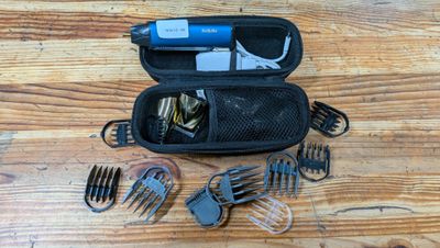une tondeuse à cheveux, des peignes, des ciseaux et d'autres objets rangés dans une trousse posée sur une table en bois