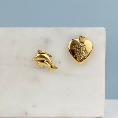 Boucles d'oreilles clous en forme de dauphin et de cœur plaquées or, posées sur une dalle de marbre