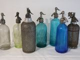 Plusieurs bouteilles en verre de différentes couleurs sont alignées sur une surface blanche.