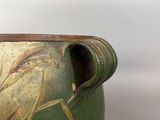 a green vase with a brown handle sitting on a white surface