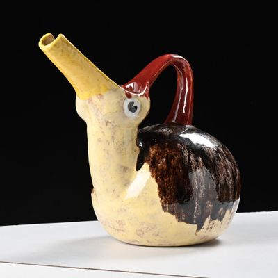 un vase marron et blanc muni d'une anse rouge, posé sur une table blanche