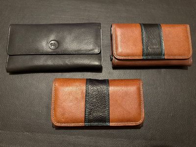 three leather wallets on a black table with a brown and black stripe