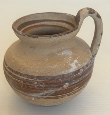 un vase marron muni d'une anse, posé sur une table blanche