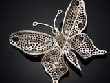 a close up of a silver butterfly broochle on a black surface