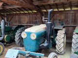 Plusieurs vieux tracteurs sont garés dans une grange où se trouve une pancarte posée par terre.