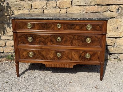 an antique chest of drawers with marble top in front of a stone wall